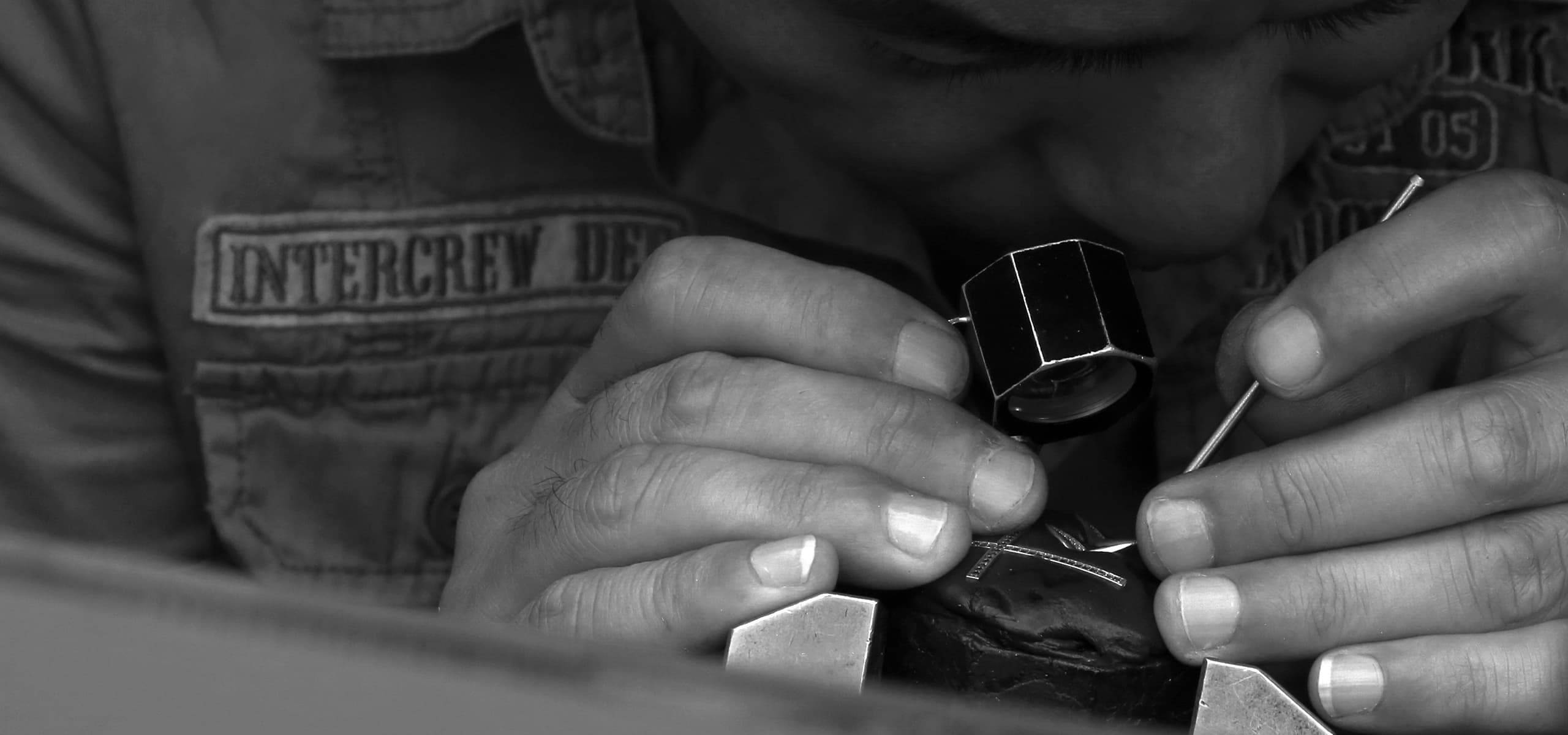 A craftsperson working on jewelry with a loupe and hand tools